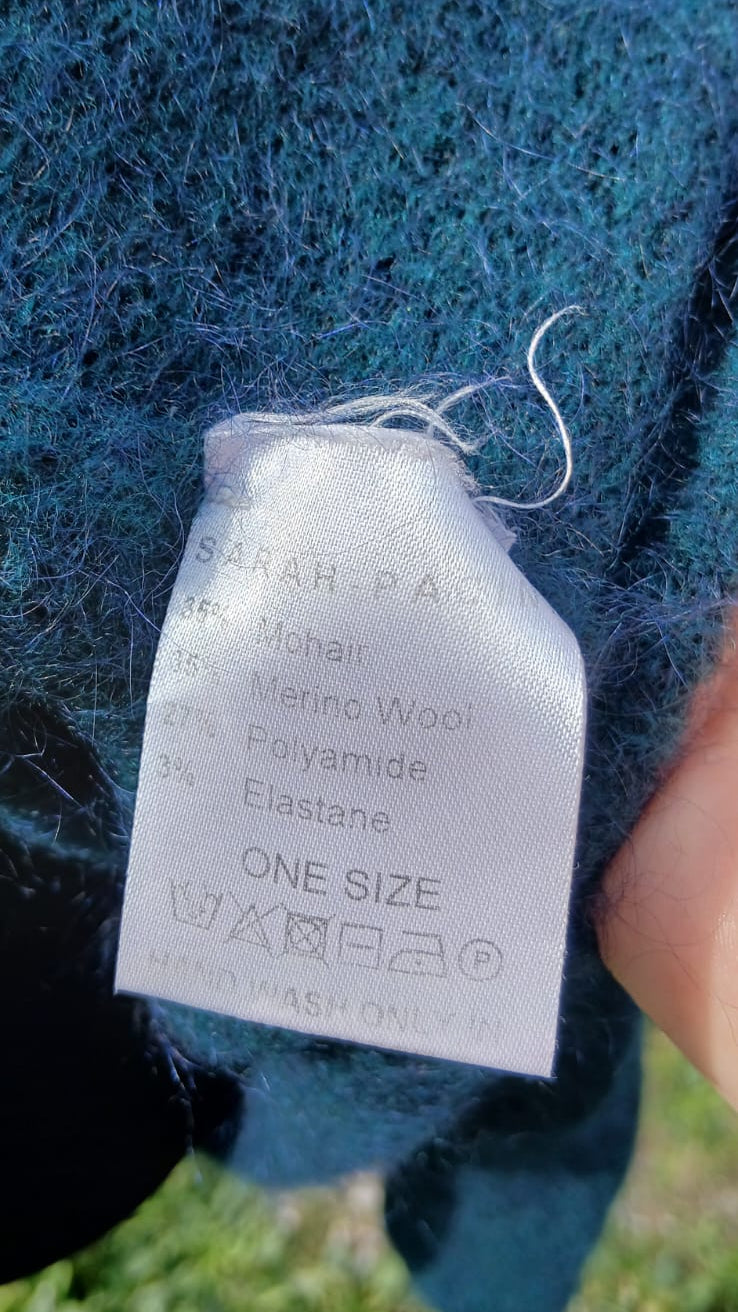 A close-up of a blue-green mohair sweater showing the inner care label.