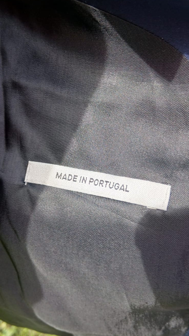 Close-up of a dark fabric garment with a white label reading 'MADE IN PORTUGAL' sewn onto the inside.