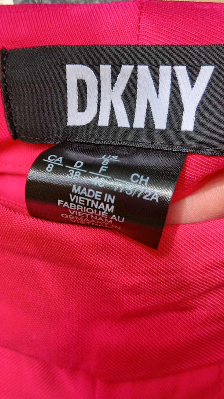 Close-up of a bright pink DKNY trousers showing the black brand label and size tag.