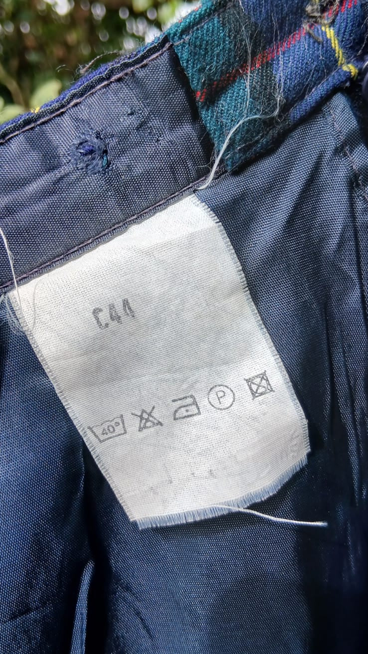 Close-up of the waistband of a plaid patterned skirt inner waistband, showing a white care label with instructions .
