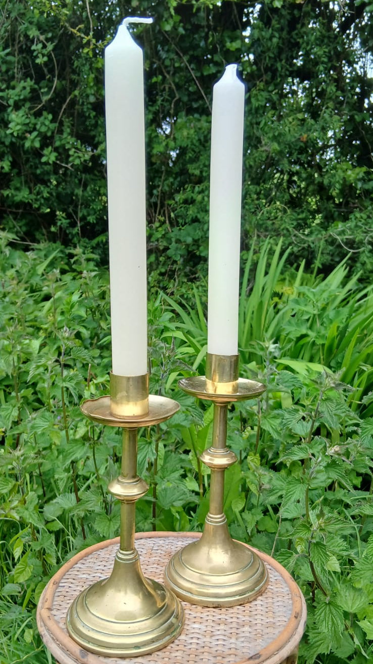 Two vintage brass candlesticks holding white taper candles