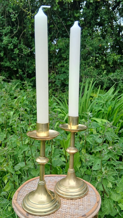 Two vintage brass candlesticks holding white taper candles