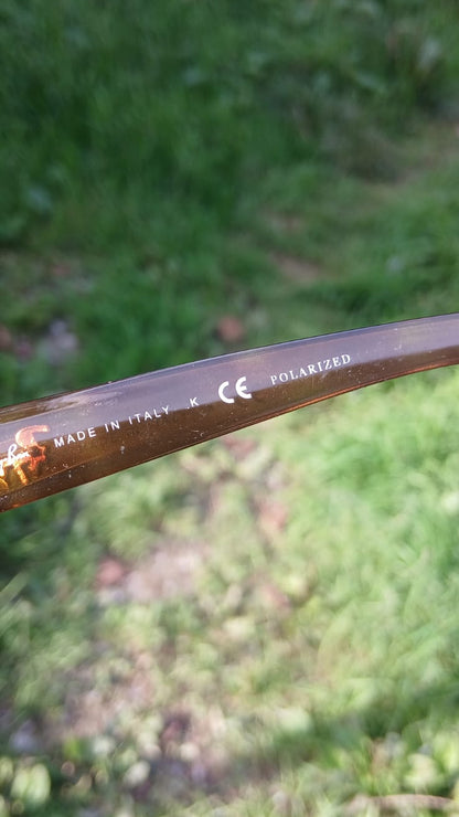 A close-up of a brown acetate arm of sunglasses with white printed text including 'MADE IN ITALY', 'CE', and 'POLARIZED'.
