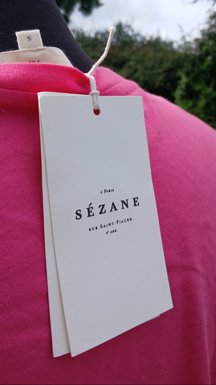 A white brand tag that reads  'SÉZANE' of a bright pink short-sleeve t-shirt featuring the words 'BACI & SPAGHETTI' printed across the chest in a dark red font.