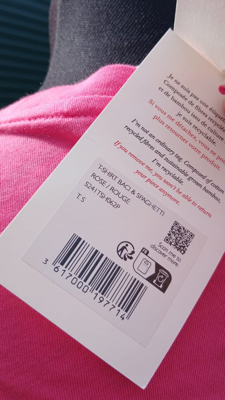 A close-up of a product tag with details of a bright pink short-sleeve t-shirt featuring the words 'BACI & SPAGHETTI' printed across the chest in a dark red font.
