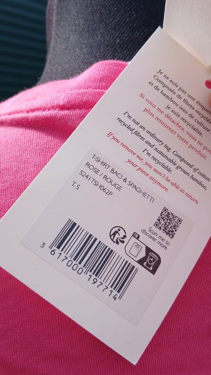 A close-up of a product tag with details of a bright pink short-sleeve t-shirt featuring the words 'BACI & SPAGHETTI' printed across the chest in a dark red font.