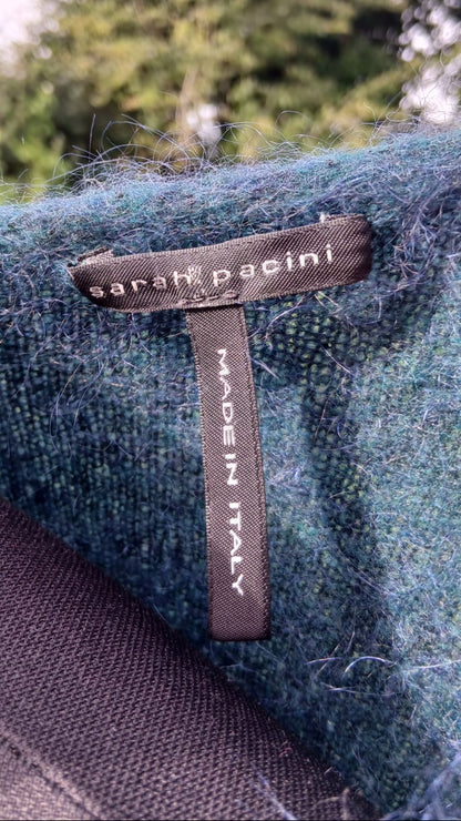 Close-up of a Sarah Pacini wool label on a textured teal blue-green wool fabric.