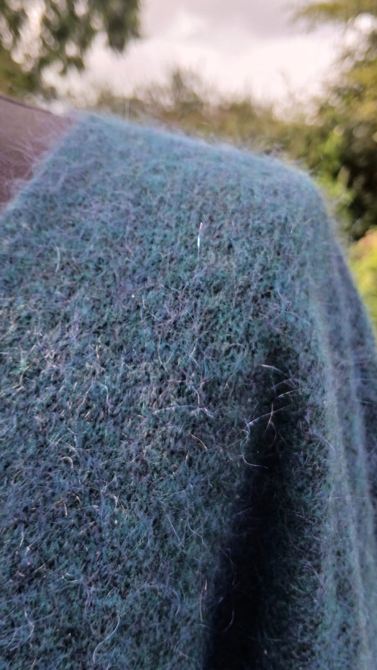 A close-up shot of a fuzzy, textured knit fabric in a muted teal blue-green colour.