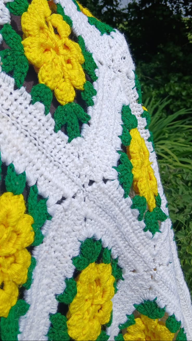 a close up on the crochet blanket showing in more detail the yellow flowers and green leaves 
