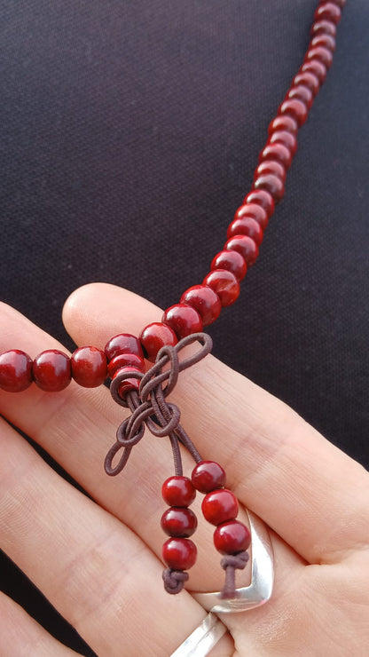 A close-up of a beaded necklace with deep red round beads and a dark brown cord knot detail.