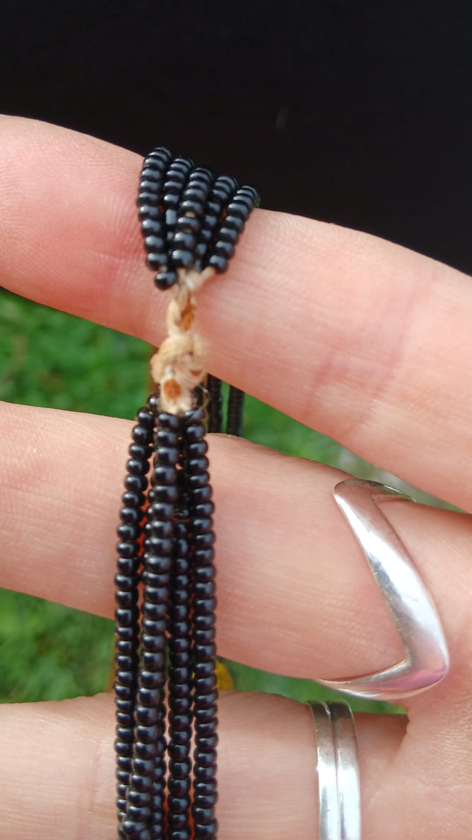 A close-up of a black beaded necklace tied with a knotted fiber cord.