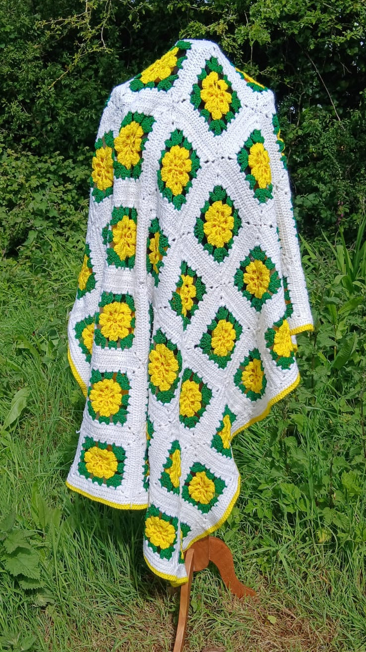 Beautiful handmade crochet blanket with yellow sunflower-like motifs over green diamons on a white base 