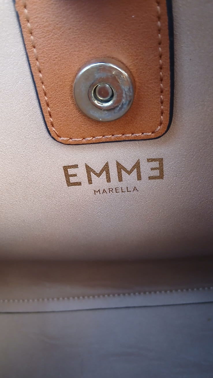 Close-up of the inside of a tan leather bag with a tan leather strap tab, a silver metal snap button, and the brand name 'EMME MARELLA' printed in gold.