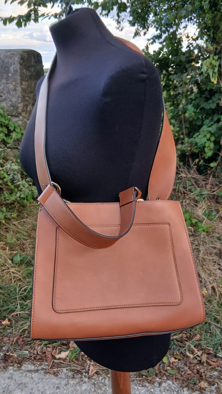 A tan leather shoulder bag with a wide top handle and a wide adjustable shoulder strap by Emme.