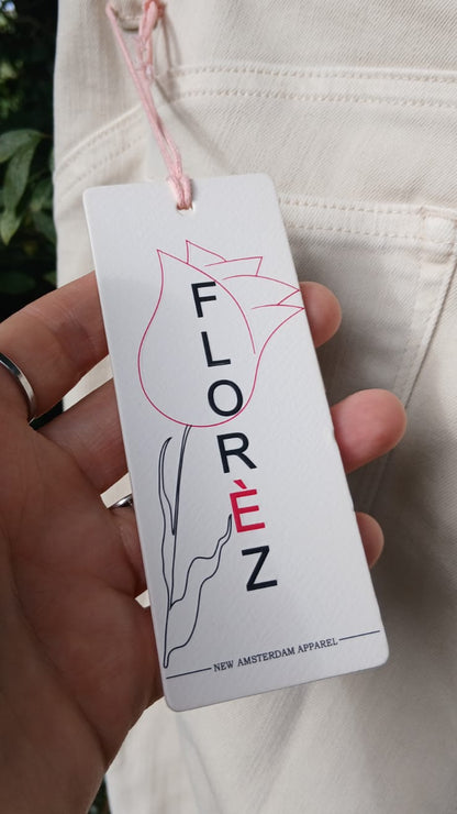 A white brand tag for FLOREZ next to a close-up of cream trousers.