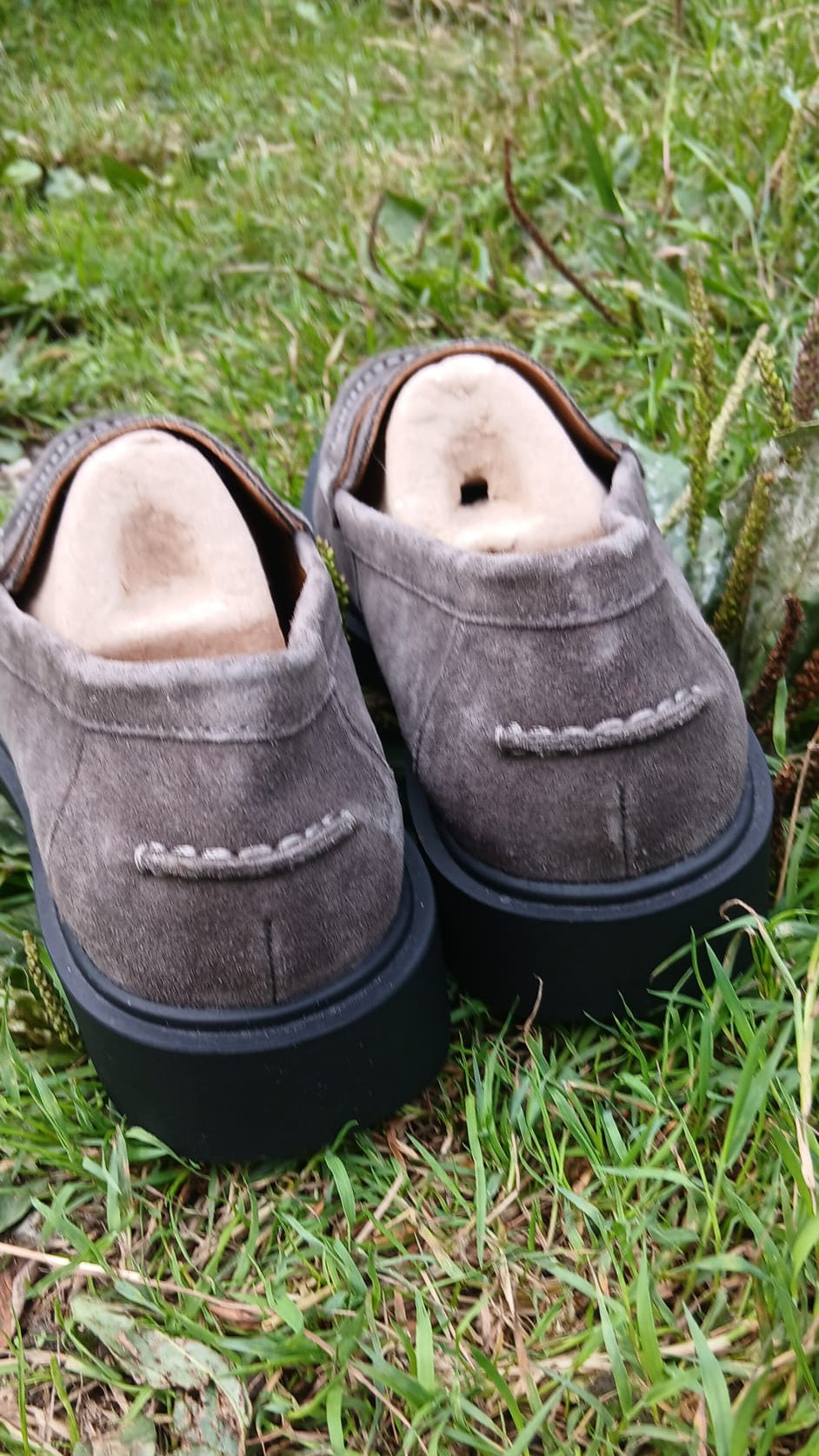 A pair of gray suede moccasins with black soles.