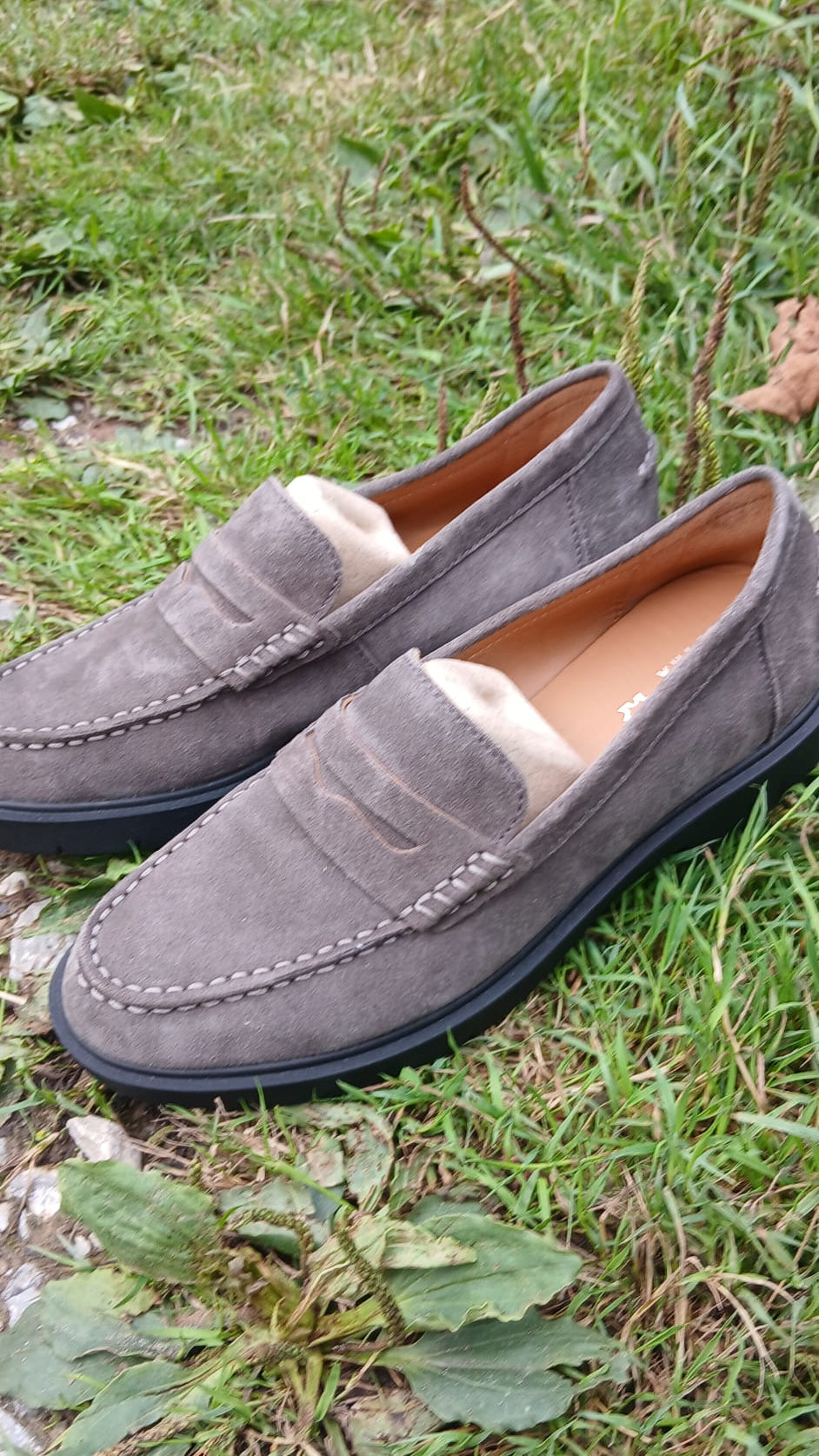 A pair of gray suede moccasins with black soles.