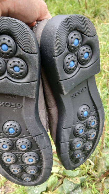 A close-up of  the soles of a pair of moccasins with visible blue and gray tread patterns and the brand name GEOX embossed.