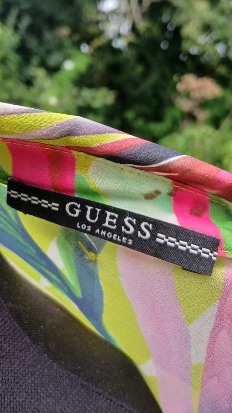 Close-up of a colorful GUESS Los Angeles label sewn onto a vibrant tropical palm printed fabric.