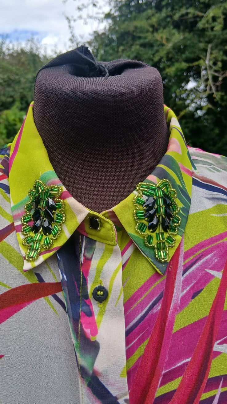 A close-up of a colorful patterned button-up shirt featuring bright lime green, pink, yellow, and blue abstract stripes with ornate green beaded embellishments on the collar.