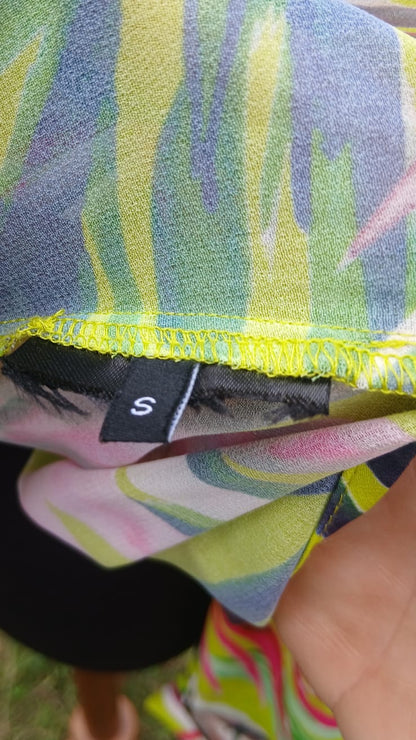 Close-up of a colorful tropical palm print shirt with a neon yellow stitched hem and a black size tag marked 'S'.