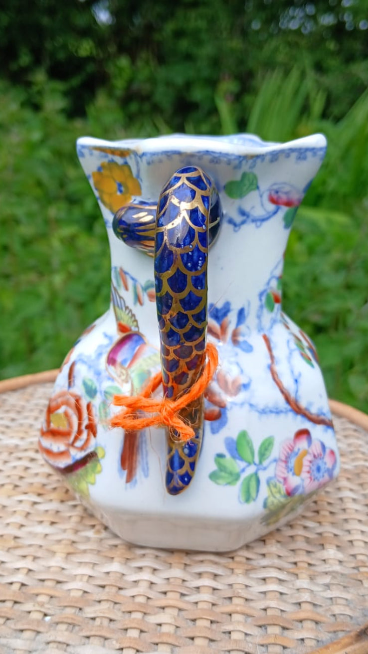 A hand-painted Mason's ironstone pitcher with a blue and gold patterned "hydra" handle and colorful floral designs on a white body.