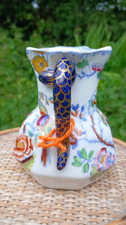 A hand-painted Mason's ironstone pitcher with a blue and gold patterned "hydra" handle and colorful floral designs on a white body.