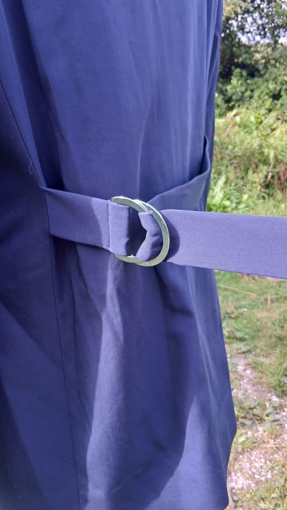 A close-up of a waist tie belt, featuring a wide strap and a silver-toned metal ring buckle.