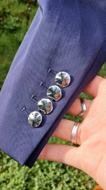 A close-up of a purple blazer sleeve, showing four decorative silver-toned buttons with a floral pattern.