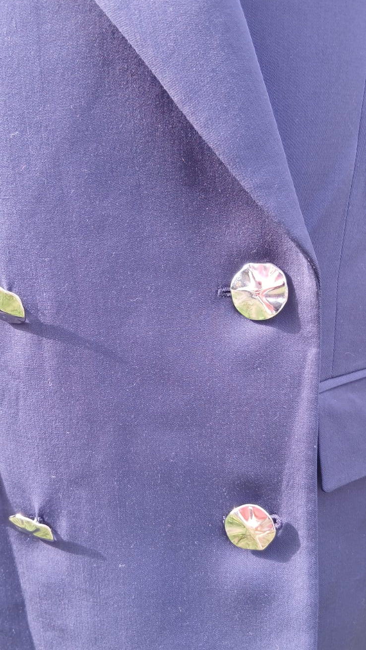 Close-up of a double-breasted blazer in a purple-blue fabric, featuring silver buttons.