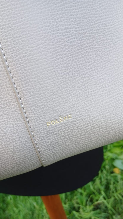 A close-up of a light beige pebbled leather handbag with gold 'POLECE' lettering.