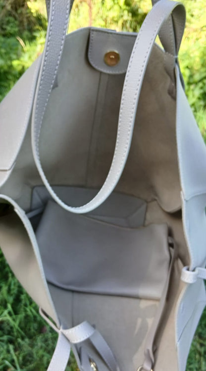 A light gray tote bag shown open. The bag has light gray straps, a gray interior, and small gold-tone hardware.