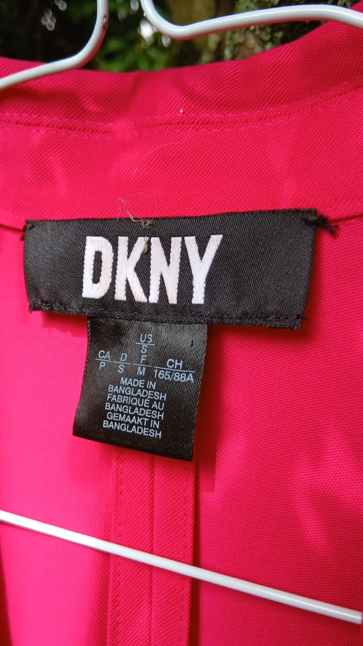 A close-up of a bright pink DKNY blazer, showing the black brand label with white lettering.