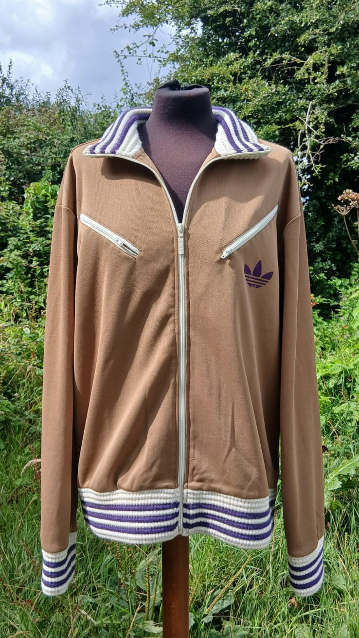 A vintage 'adicolor 70s' tan Adidas track jacket with white and purple striped accents on the collar, cuffs, hem, and zipper details.