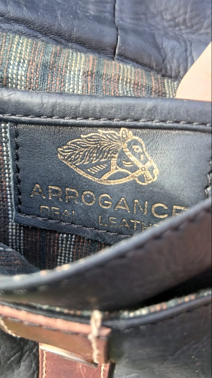 Small vintage Arrogance black leather crossbody bag with cognac brown trim, front flap buckle accent, and striped lining
