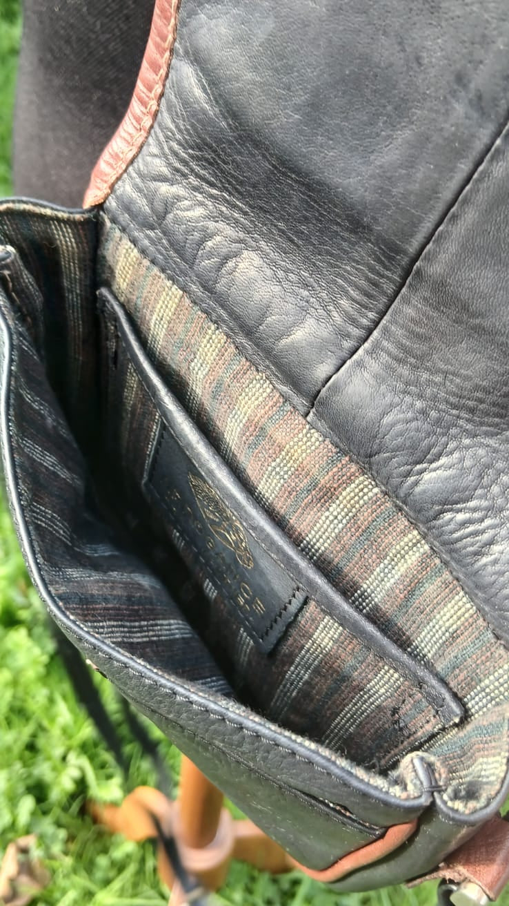 Small vintage Arrogance black leather crossbody bag with cognac brown trim, front flap buckle accent, and striped lining