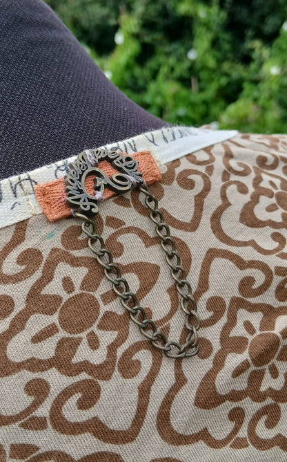 A close-up of a brown and beige patterned fabric top with a decorative chain with the brand name "Angels Never Dies" near the neckline.