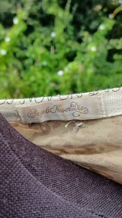 Close-up of a top's collar showing a beige brand label that reads 'Angels Never Dies'.