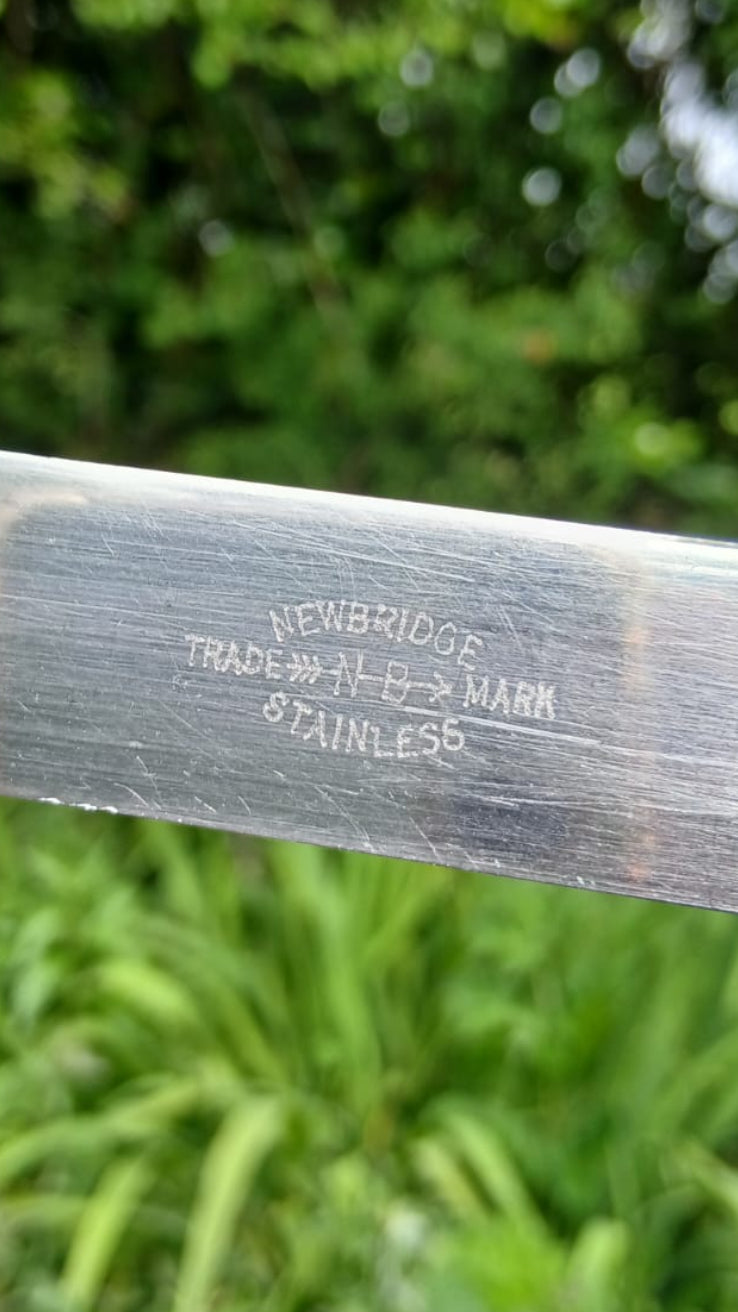 A close-up of a stainless steel sword blade showing stamped newbridge trademark text.