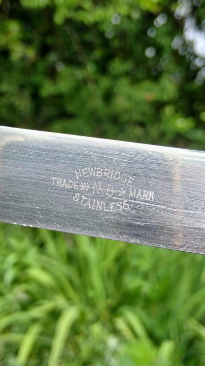 A close-up of a stainless steel sword blade showing stamped newbridge trademark text.