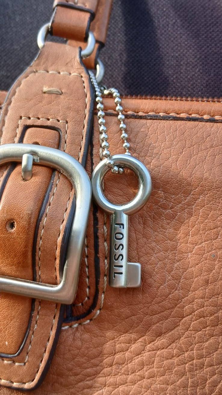 A close-up of a brown leather bag with a silver-tone metal key charm engraved with the brand name 'FOSSIL'.