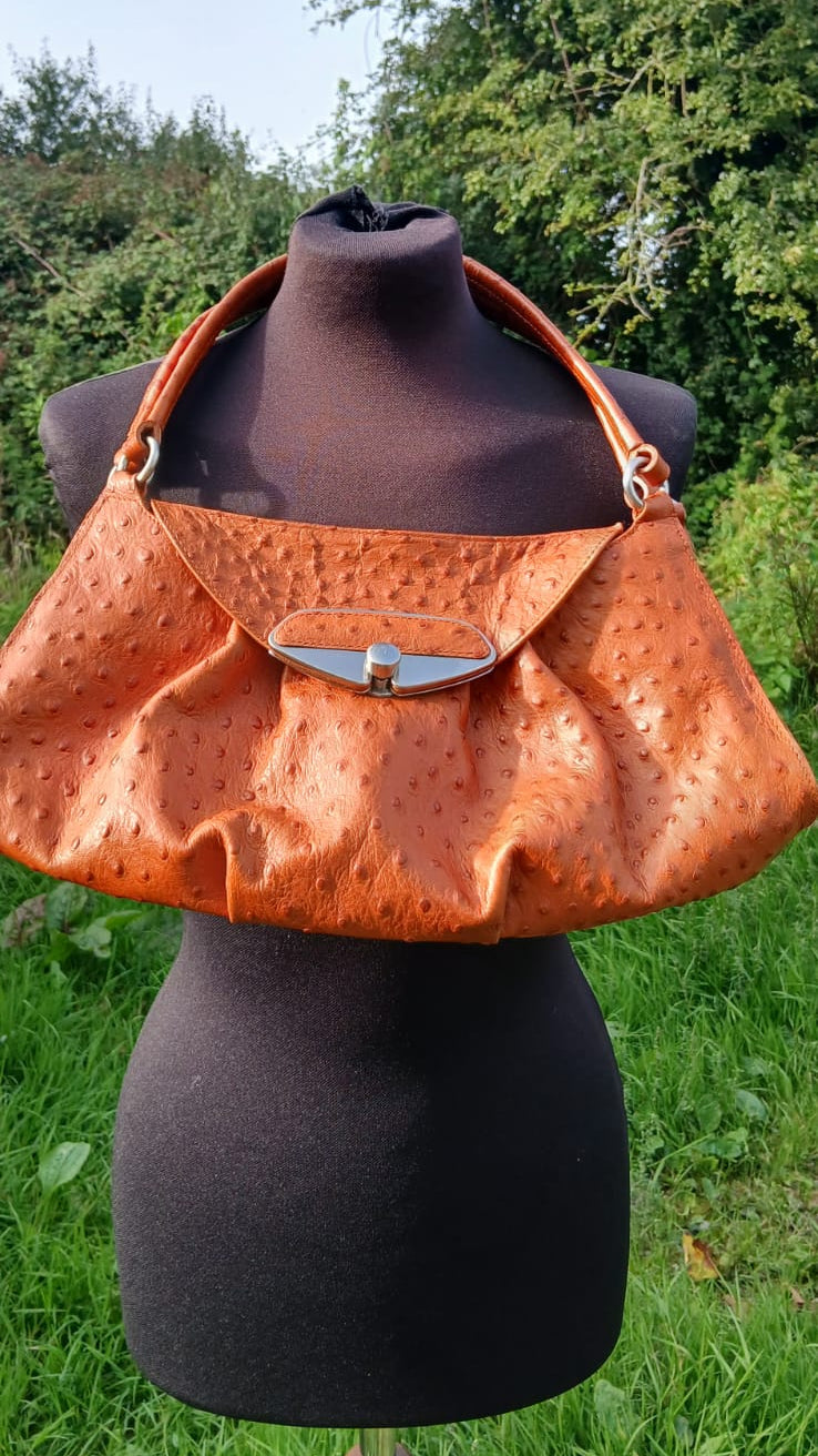 This Italian-made Furla handbag is crafted in rich burnt orange ostrich-embossed leather, this shoulder bag features elegant gathered pleating, dual flat leather shoulder straps, a spacious tonal textile logo interior lining and a sleek silver-tone push-lock closure on the front flap.