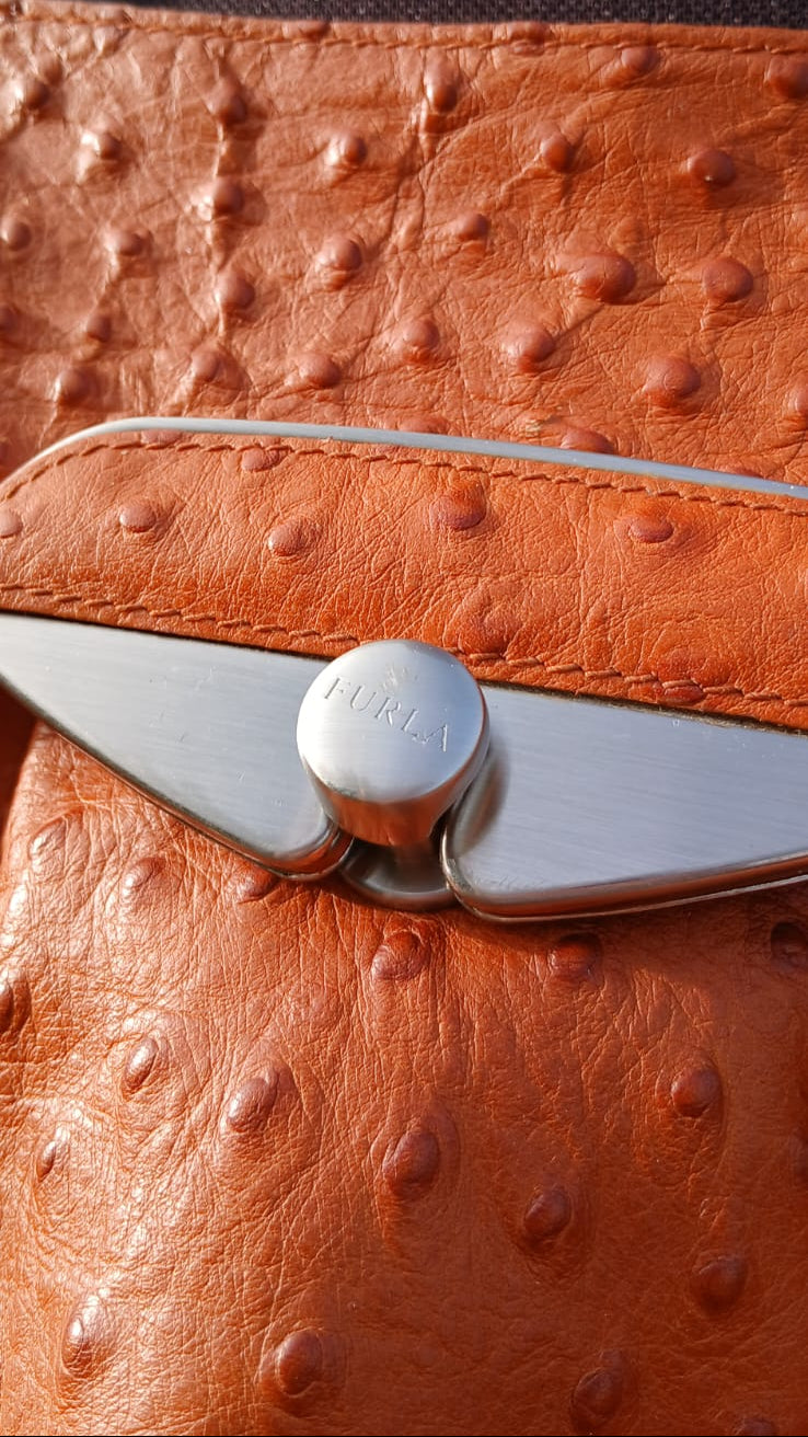 This Italian-made Furla handbag is crafted in rich burnt orange ostrich-embossed leather, this shoulder bag features elegant gathered pleating, dual flat leather shoulder straps, a spacious tonal textile logo interior lining and a sleek silver-tone push-lock closure on the front flap.