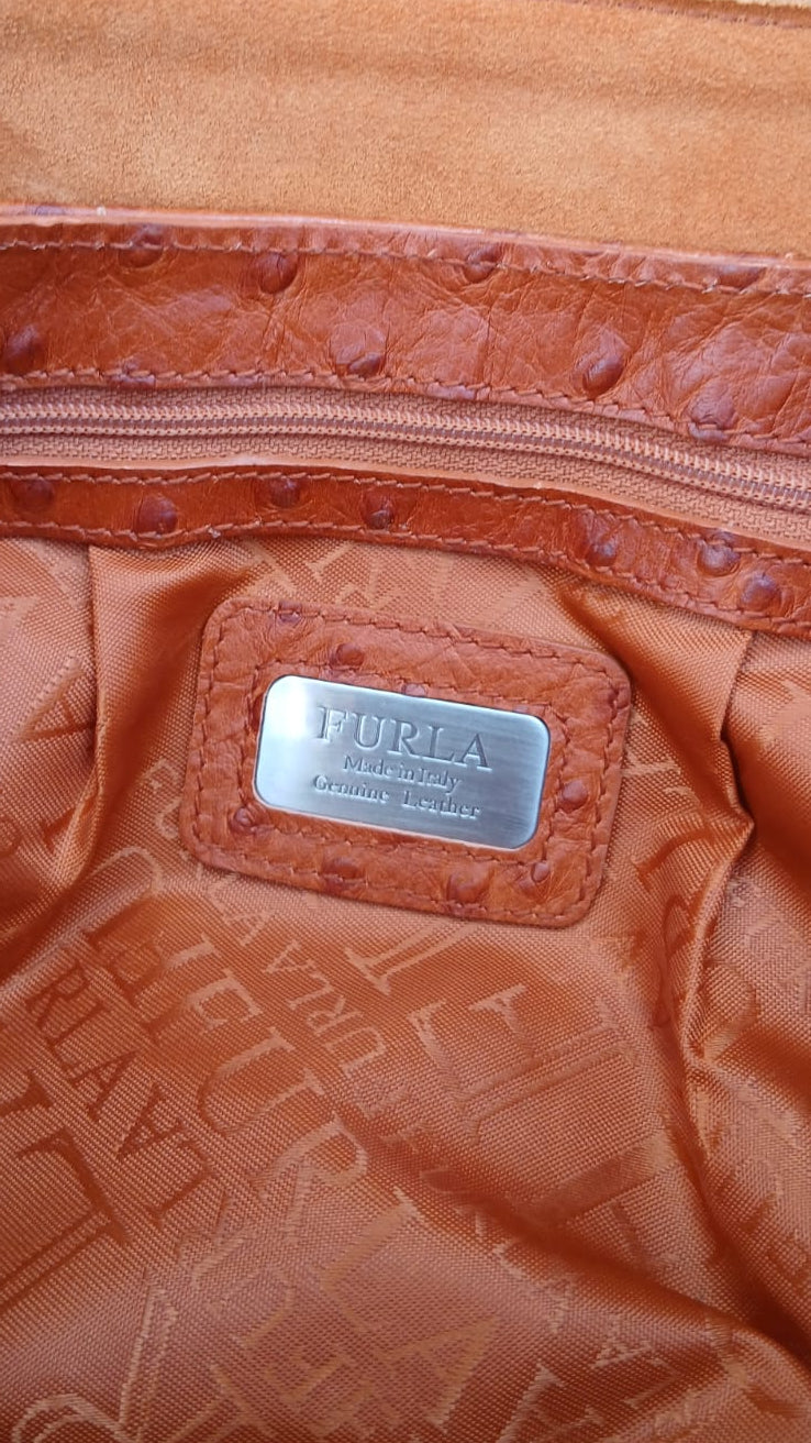 This Italian-made Furla handbag is crafted in rich burnt orange ostrich-embossed leather, this shoulder bag features elegant gathered pleating, dual flat leather shoulder straps, a spacious tonal textile logo interior lining and a sleek silver-tone push-lock closure on the front flap.
