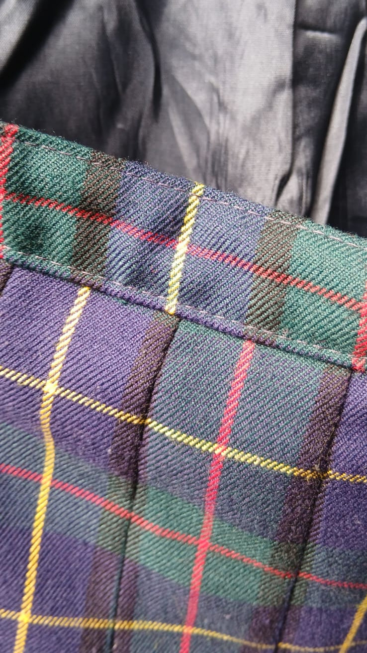 Close-up of a tartan plaid fabric with blue, green, yellow, and red lines, showing pleats .