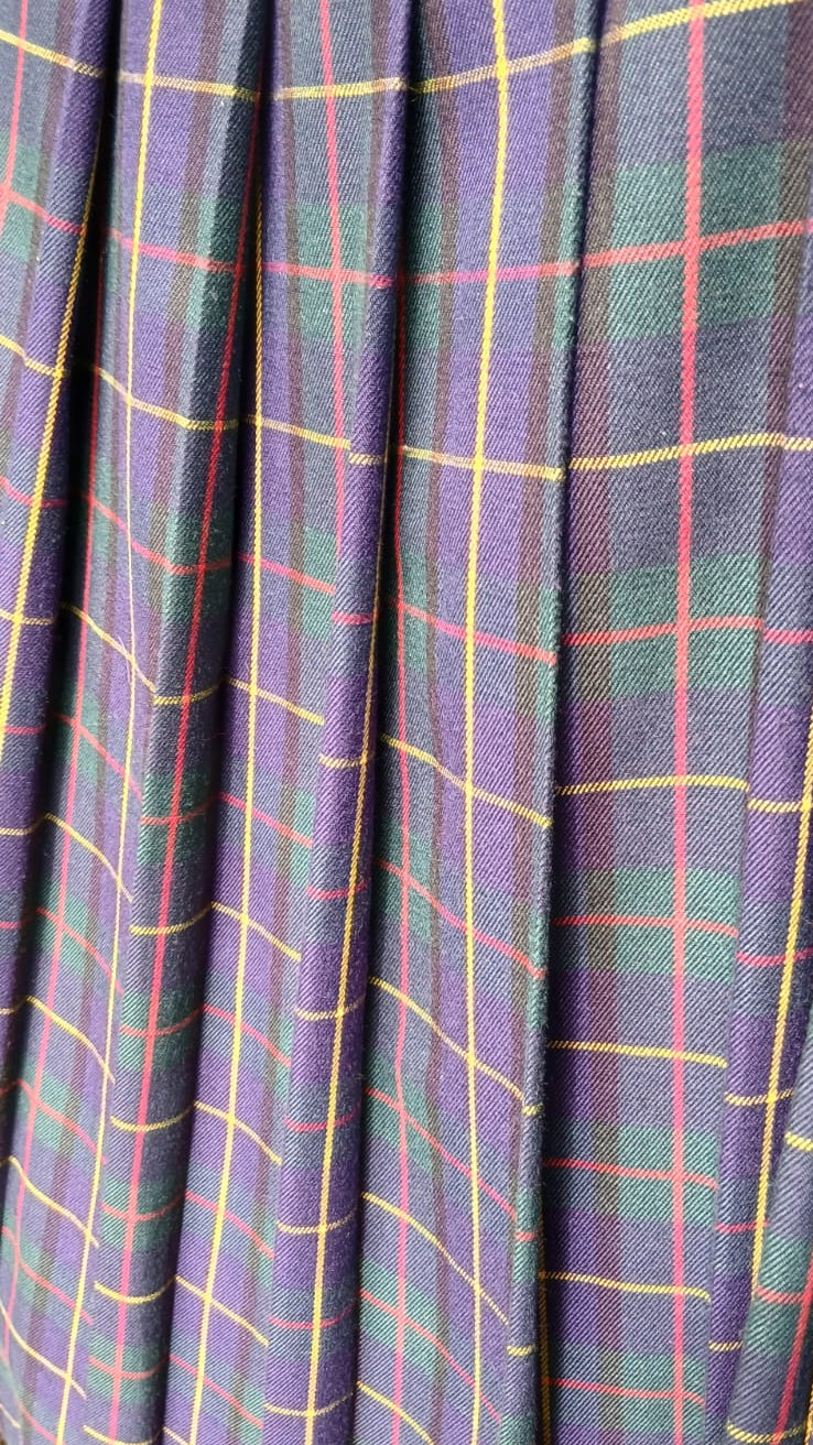 Close-up of a pleated fabric surface with a tartan plaid pattern in blue, green, red and yellow lines.