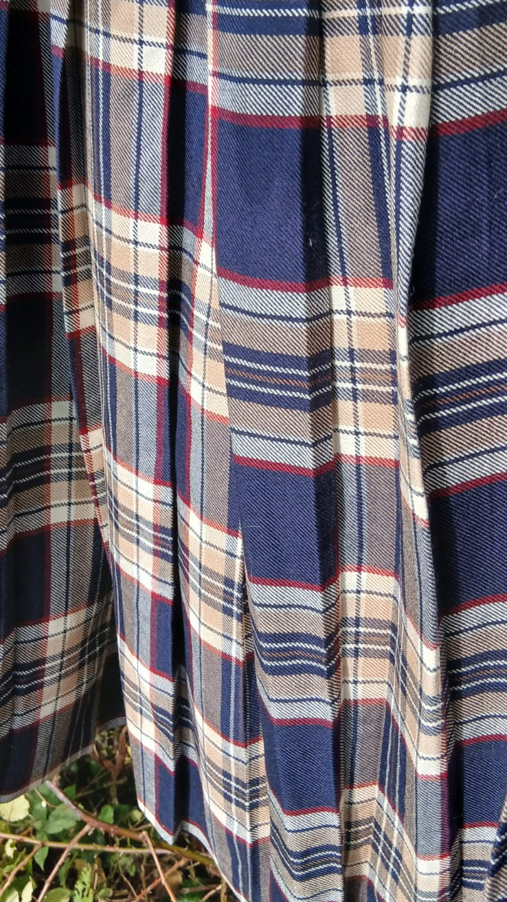 A close-up of a pleated skirt in a blue, beige, and red plaid pattern from the brand Seven Pride.