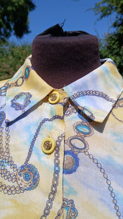 A close-up of a collared button-front shirt with a pale yellow base and a blue jewelry chain-link pattern and yellow buttons with gold accent.