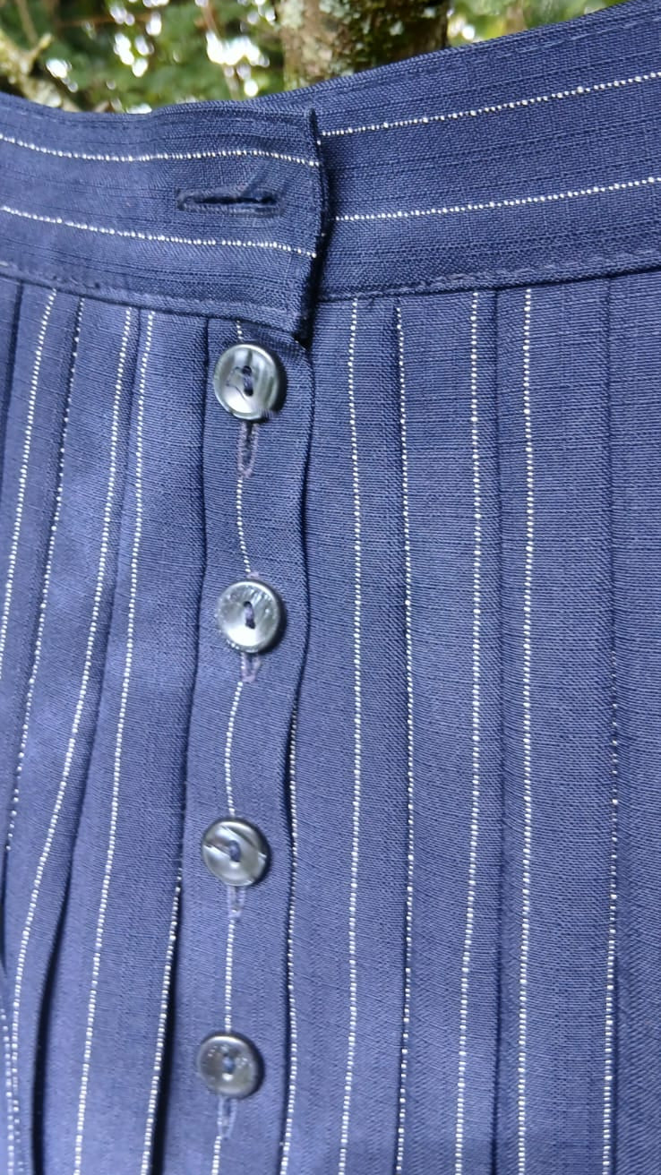 Close-up of a St Micheal navy blue skirt with thin white vertical pinstripes and button-front closure.