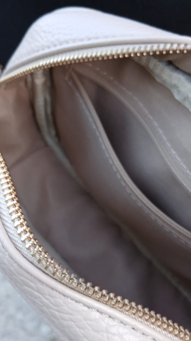 Close-up of a light beige pebbled leather bag interior with a gold zipper and multiple internal compartments.